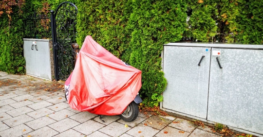motorcycle under a tarp parked on a sidewalk outside of a gate